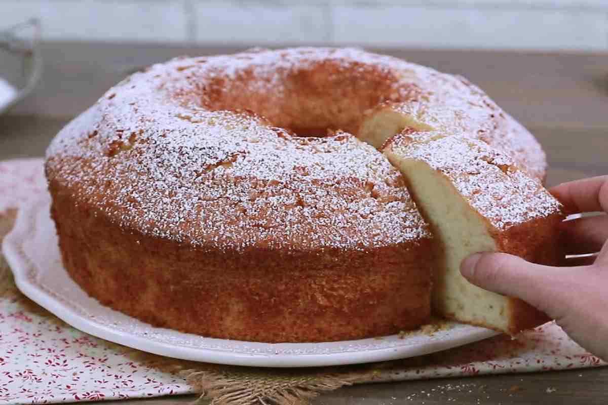 Una mano prende una fetta da un ciambellone intero