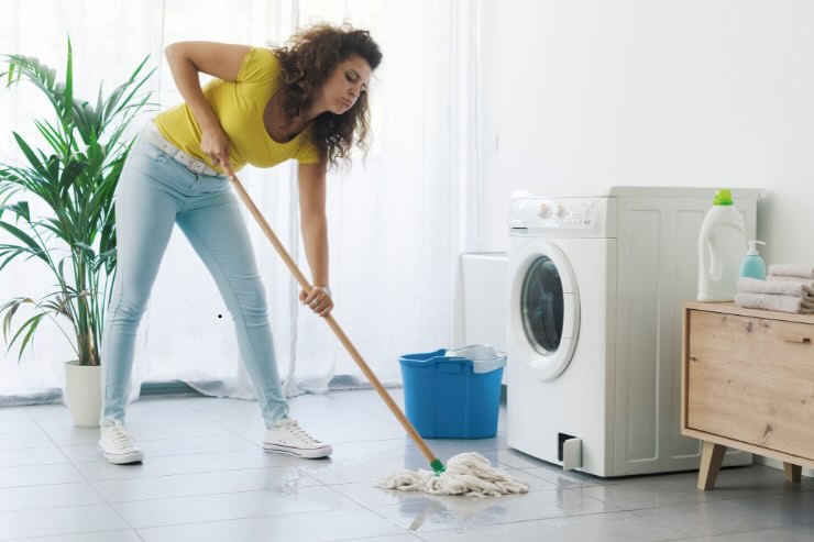 donna con maglia gialla che pulisce acqua da terra vicino alla lavatrice